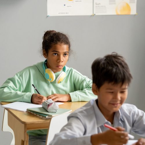 Cute African-American schoolgirl looking at blackboard or teacher at lesson